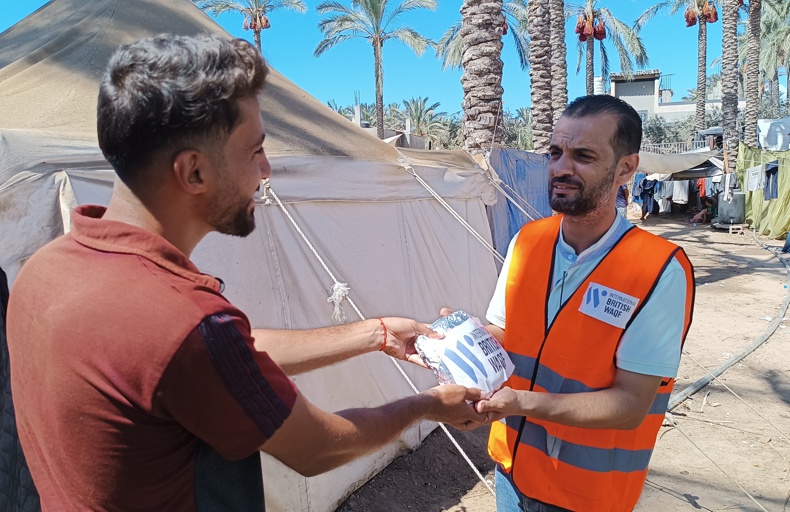 الصدقة في العشر الأواخر من رمضان متطوع يرتدي سترة برتقالية يوزع وجبة طعام على رجل في مخيم للاجئين.