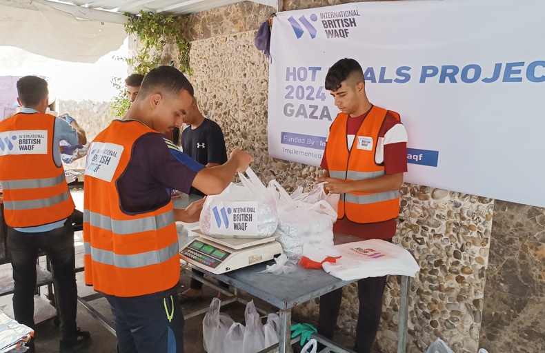 فوائد الوقف الخيري متطوعون يرتدون سترات برتقالية يعبئون ويوزعون أكياس الطعام ضمن مشروع وجبات ساخنة إنساني.
